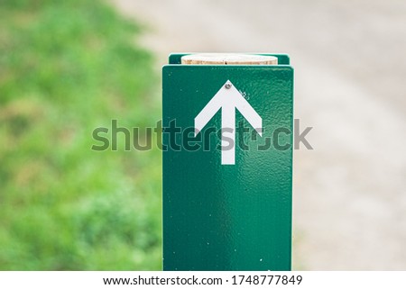 White directional arrow on a green wooden post.