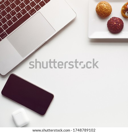 Flat lay photo of office desk with laptop, phone, headphones, snack on the plate and coffee. Square format