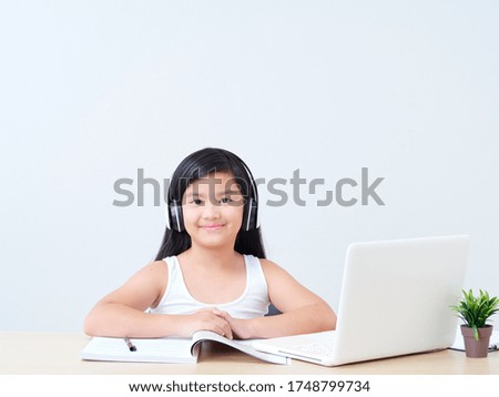 Little girl in headphones and doing online class with laptop at home.