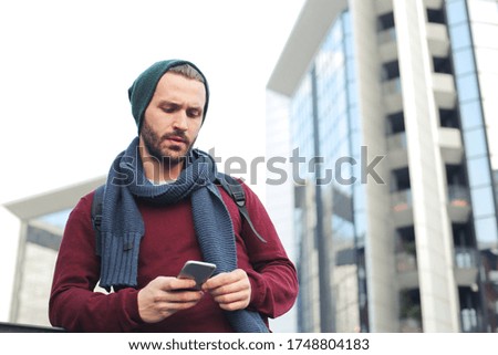 A low angle shot of a young male checking his phone on the street