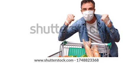 Protected man with mask and gloves with closed fists hands with success gesture with a cart full of food isolated white