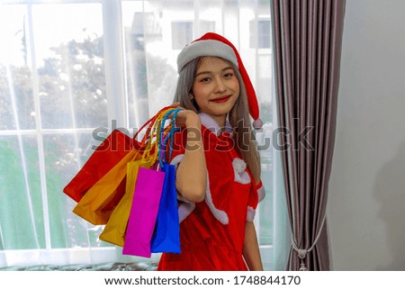 Beautiful girl wearing a Santa dress holding colorful shopping bag in the Christmas festival with white curtain background