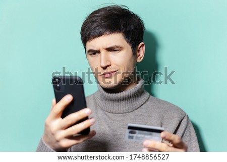 Studio portrait of young guy using smartphones and credit card on background of aqua menthe color.