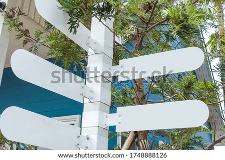 A white blank directional sign with background of tree and wooden house