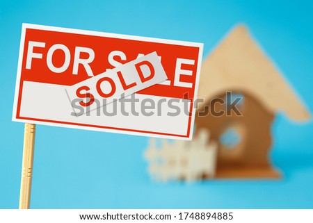 Real estate agent for sale sign with sold sticker and house in background