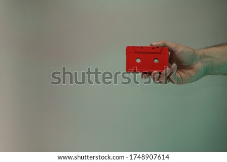 Hand holding red audio cassette tape in the color light. Beautiful minimal in neon light. Minimalism retro style concept. Background pattern for design. 
