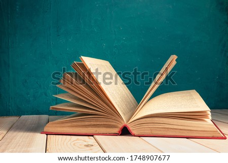 Beautiful ancient open old book on a red  wooden table and dark-green wall background behind.