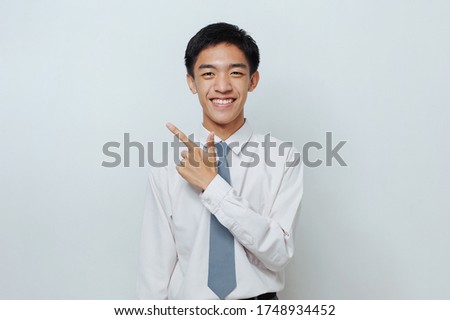 Indonesian Senior Student wearing uniform pointing at copy space or blank space, isolated on grey background