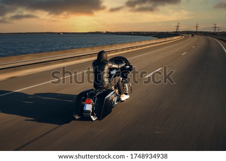 
A motorcycle driver rides alone on an asphalt highway. Biker in motion on an empty road during sunset. Riders go fast on the autobahn. Motion blur  Royalty-Free Stock Photo #1748934938
