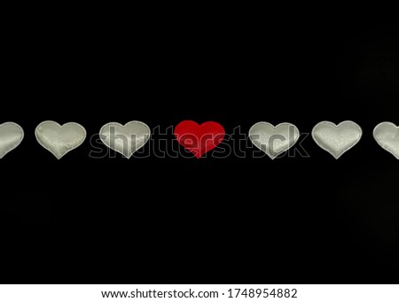 White hearts in a row with a central red heart on a black background. Concept: you are not like everyone else, special, true love. Blank for card with your text. Image with selective focus on the cent