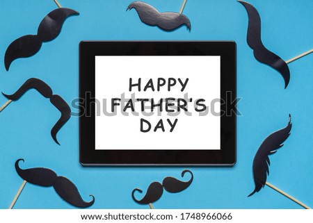 Various black photo booth props moustaches and tablet screen on blue background. Text HAPPY FATHER'S DAY, greeting card. Flat lay, top view