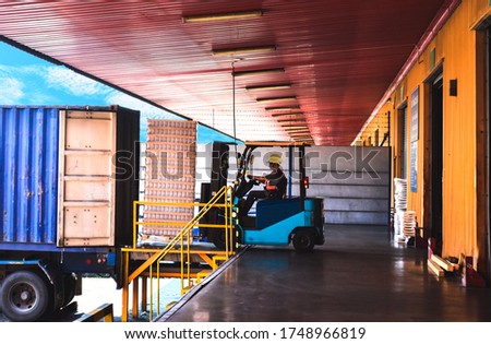 Forklift stuffing-unstuffing pallets of cargo to container on warehouse leveler dock. Royalty-Free Stock Photo #1748966819