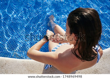 brunette girl looks at her smart watch in the pool. Sport concept, modern and healthy