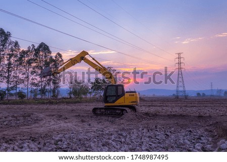 Yellow excavator moving soil and sand on construction site with sun rise.