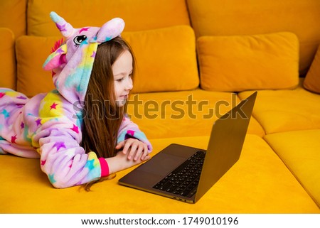 little girl in kigurumi lies at home on a couch with a laptop. children's distance education. self-isolation