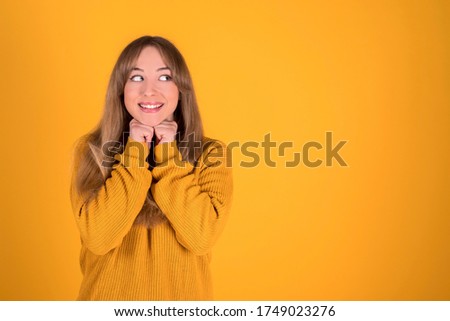 Happy woman with hands on chin looking aside yellow background
