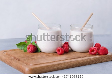 Two glasses of raspberry milkshake on wooden background