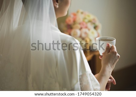 A bride's morning, coffee for breakfast, transparent white peignoir and gentle hands. A picture of an elegant female hand with fine manicure pulling to a perfect cup of coffee