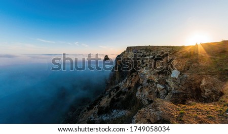 Selective focus. Scenery with shining sun in the sky over the misty Sea coast at sunset. Clouds and fog over the rocky seashore. Copy space. The concept of calmness, silence and unity with nature.