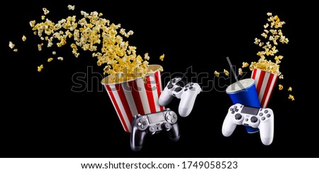 Flying popcorn, blue cup of soft drink and video game joystick gamepad isolated on black background. Concept of refreshments in cinema or watching movies