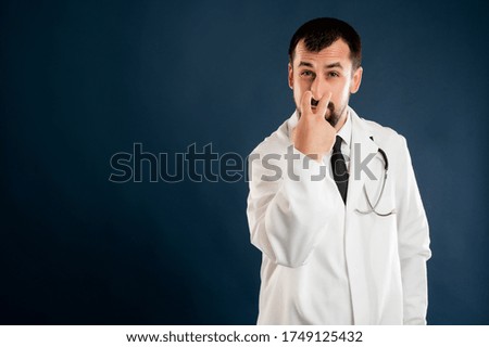 Portrait of male doctor with stethoscope in medical uniform doing look into my eyes or pay attention at me gesture posing on a blue isolated background.