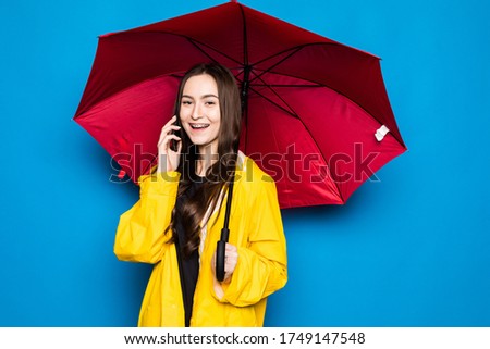 Happy pretty smiling young woman with umbrella using smartphone in autumn day over colorful blue background