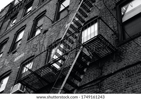 Black-and-white photo of a brick building facade and its fire escapes in New York City