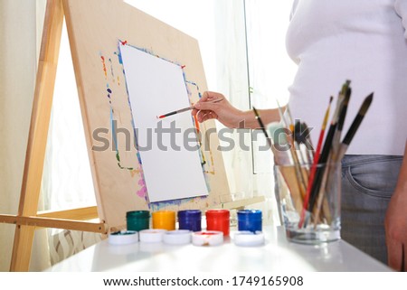 artist’s hand paints on an easel with a brush