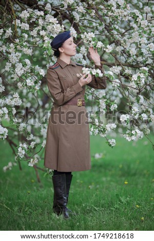 A young female pilot in uniform of Soviet Army pilots during the World War II. Military shirt with shoulder straps of a major and a beret. In spring blooming apple orchard