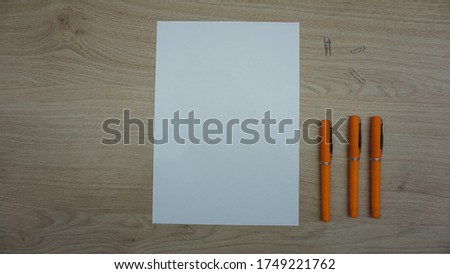 blank paper against wooden table and orange pens