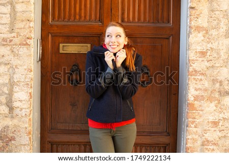Alone happy independent caucasian adult beautiful woman having cold standing outside near the wooden doors of her home ready to enjoy and start the day outdoors. Stylish people traveling concept