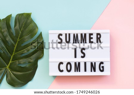 'Summer is coming' text on a lightbox on color background, top view. Flat lay, overhead, from above. Copy space.