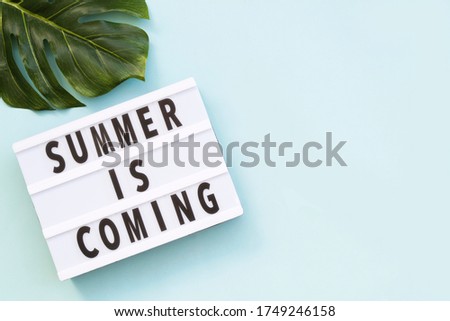 'Summer is coming' text on a lightbox on blue background, top view. Flat lay, overhead, from above. Copy space.