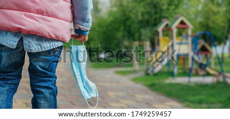 Close up of little girl take off and holding protective face mask looking at the open playground after the end of quarantine. Pandemic COVID-19 is over concept. Pnoramic background.