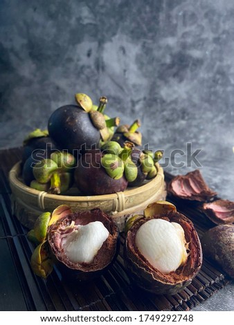 Fresh ripe mangosteen fruits and cross section showing the thick purple skin and white flesh over dark background. 
