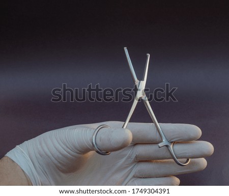 Hand-held stainless steel surgical forceps with white gloves