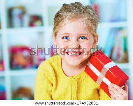 Happy little girl hold red gift. Home portrait.