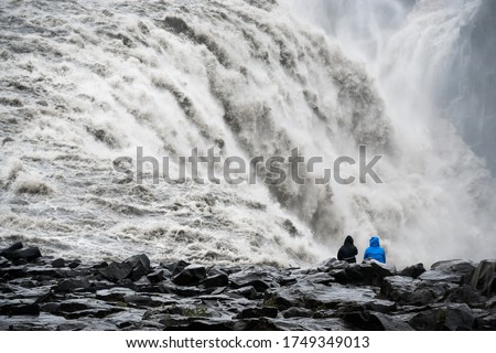 Close up of a huge raging icelandic waterfall with a black rocky shore in the foreground