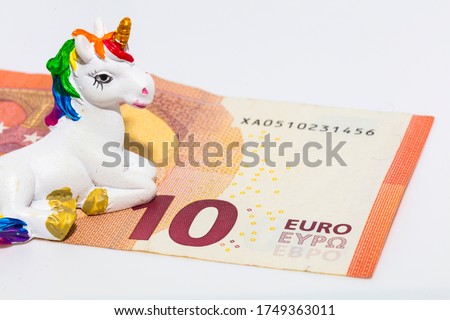 Closeup photo on a small cute white and rainbow unicorn sculpture together with a 10 Euro banknote, the official currency of the European union.