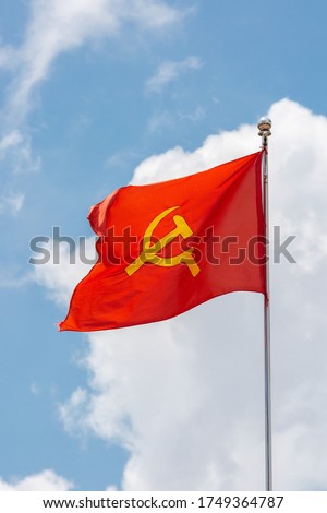 A red flag with communist symbols of a sickle with a hammer flying in a blue sky