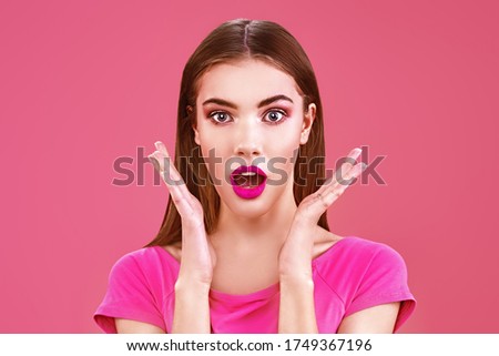 Beautiful young girl with bright makeup looks at the camera with big eyes and is surprised. Portrait on a pink background. Beauty, make-up and cosmetics concept.