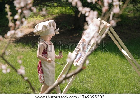 Little girl in nature paints on an easel under a blooming cherry