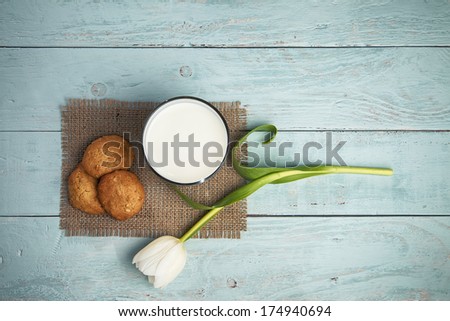 glass of milk, home baked cookies, and tulip on blue wooden table