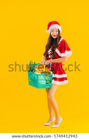 Portrait beautiful young asian woman wear christmas clothes hat with grocery basket shopping bag from supermarket store on yellow isolated background