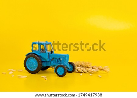 Toy blue retro tractor collects a crop of wheat on a yellow background. Copy space.