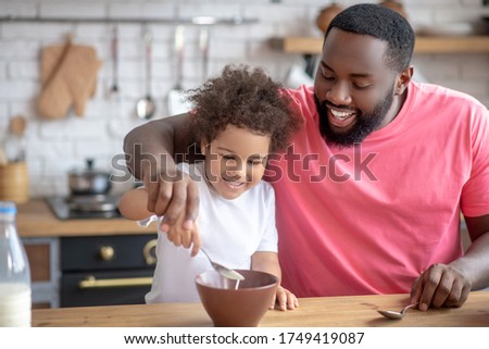 Breakfast ready. African american bearded man stirring milk in his daughters plate Royalty-Free Stock Photo #1749419087