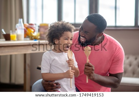 Singing songs. Cute kid with curly hair and her father holding spoons and singing a song Royalty-Free Stock Photo #1749419153