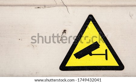 Yellow security camera sticker. Painted wooden facade. Procedures and compliance with regulations. Weather resistance