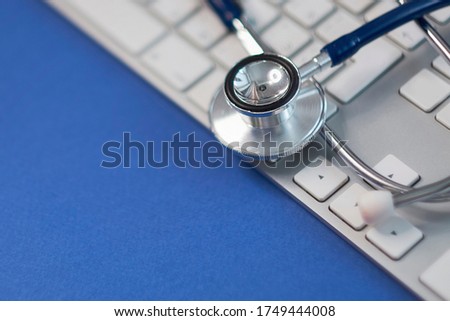 Silver stethoscope lying down on white keyboard, toned blue. stock image photo