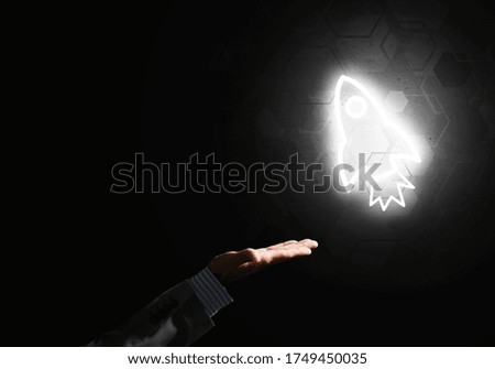 Rocket glowing icon and businessman hand on dark background